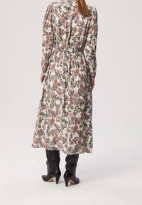 Blommig klänning med lång ärm och inringad midja, med vit botten och färgglada blommönster. Matchas med knähöga svarta klackstövlar.