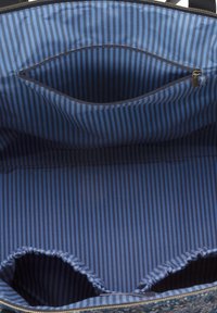 Binnenkant van een stoffen boodschappentas met textuur, voorzien van blauwe en marineblauwe verticale strepen. Bevat een ritszak en twee open compartimenten aan de onderkant.