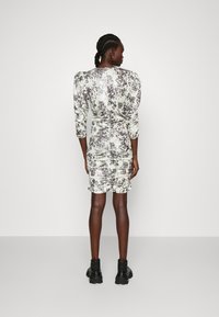 Blumenmuster-Minikleid in Hellgrün und Grau. Merkmale sind gepuffte Schultern, Rüschendetails und eine figurnahe Silhouette. Schwarze Knöchelstiefel.