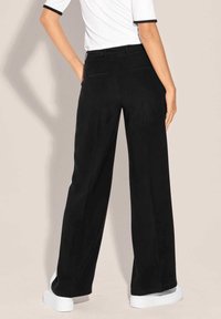 Zwarte wijde broek gemaakt van een gladde stof. Heeft een middelhoge taille, twee achterzakken en een nette, stijlvolle look. Draag het met witte sneakers.