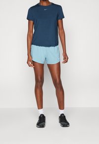Camiseta atlética de color azul marino con mangas cortas y cuello redondo, combinada con pantalones cortos de color azul claro. Zapatillas de correr negras y calcetines blancos visibles.