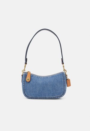 Mała niebieska torba na ramię z denimu z czarnym paskiem, brązowym skórzanym uchwytem suwaka i przymocowaną skórzaną metką na białym tle.