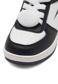 Čierno-biele tenisky s bielymi šnúrkami prevlečenými cez okrúhly biely zámok na šnúrky v prednej hornej časti.