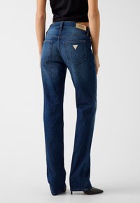 Donkerblauwe denim jeans met een rechte pijp, voorzien van een driehoekig logovlekje op de achterzak en subtiele stikseldetails.