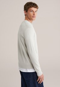 Pull en maille gris clair avec un col rond, des manches longues et des poignets côtelés. Associé à un jean foncé, affichant une texture lisse.