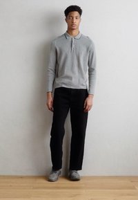 Chemise polo grise à manches longues avec col, associée à un pantalon noir et des chaussures grises. Design minimaliste, couleurs neutres et coupe classique.