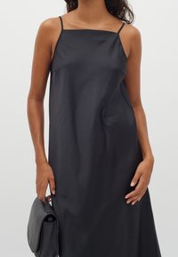 Czarna sukienka na ramiączkach z cienkimi paskami, wykonana z gładkiego materiału. Krój jest prosty, z delikatnym marszczeniem oraz prostym, minimalistycznym stylem.
