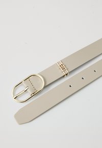 Beige leren riem met een goudkleurige metalen gesp en accent. Beschikt over een gladde textuur met meerdere verstelgaten.