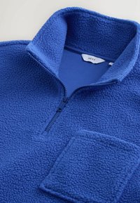 Blå fleece quarter-zip pullover med en tekstureret overflade, der har en frontlomme og en opretstående krave. Lynlås lukning ved halsen.