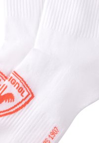 Calcetines de algodón blancos con textura acanalada y detalles del logo en naranja. Presentan un talón y puntera reforzados para mayor durabilidad. Acabados con el nombre de la marca.