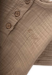 Tissu beige à tissage texturé, comportant quatre boutons ronds en bois et un détail de logo brodé.