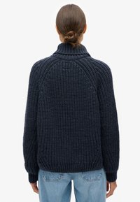 Granatowy sweter z dzianiny z wysokim kołnierzem, ściągaczami na mankietach i dole. Charakteryzuje się grubą fakturą i rękawami raglanowymi, zaprojektowany z myślą o komforcie.