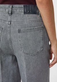 Gray denim jeans with a smooth texture, featuring a dark leather patch on the waistband and two back pockets.