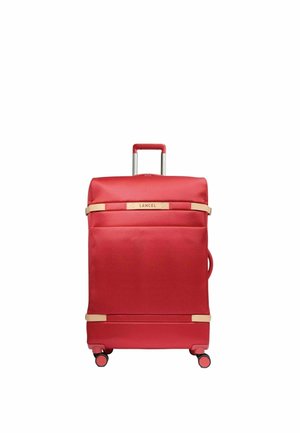 Valise à roulettes souple rouge avec une poignée téléscopique, quatre roues, des sangles beiges et le logo "Lancel" à l'avant.