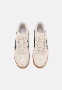 Beige sneakers med svarta accenter, snören och perforerad tå. Utrustad med en sula av gummi och en logotyp på tungan. Släta och strukturerade material.