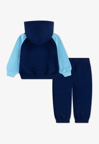 Granatowy hoodie z jasnoniebieskimi rękawami i kapturem, z elastycznymi mankietami. Pasujące granatowe spodnie dresowe z elastycznym pasem.