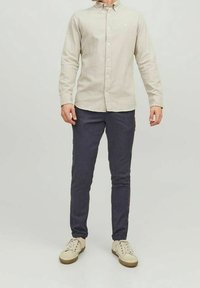 Vaaleanbeige nappikauluspaidat, tummansiniset slim-fit-housut ja beiget lenkkarit. Kankaan tekstuuri, kaulus ja hienovarainen logoakseli.