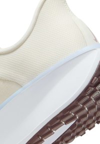 Light beige sneaker with a textured mesh upper, white midsole, and brown rubber outsole featuring a patterned tread. Subtle branding detail.
