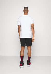 White short-sleeve t-shirt, black shorts, black sneakers with red accents, and red-striped socks. Plain, casual design with textured shorts.