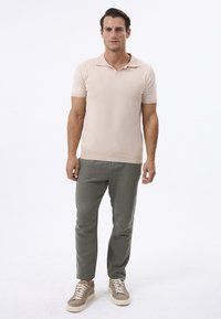 Polo shirt rosa chiaro con colletto, maniche corte e orlo a costine, abbinato a pantaloni verde oliva e sneakers beige.