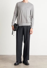 Grijze gebreide trui met een ronde hals, gecombineerd met loszittende zwarte broek en zwarte schoenen. De outfit heeft een minimalistisch ontwerp.