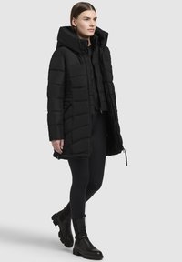 Svart puffjacka med huva, med quiltat mönster, dragkedjestängning och sidofickor. Bärs med svarta leggings och ankelboots.