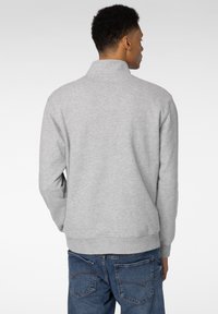 Grå hettegenser med høy krage og ribbestrikkede mansjetter, med en myk tekstur. Brukt sammen med blå denimjeans, vist bakfra.