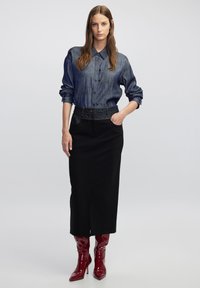 Spijkerblouse met een kraag en knoopsluiting, gecombineerd met een zwarte kokerrok met een vooraanzichtsplitsing, aangevuld met glanzende rode kniehoge laarzen.