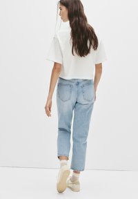 Világoskék farmernadrág laza szabással, hajtott szegéllyel és klasszikus ötlovas zsebekkel, fehér, rövidített hosszúságú pólóval és bézs tornacipővel párosítva.