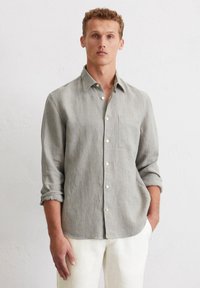 Leichtes, vertikal gestreiftes Hemd in Grau und Creme, mit einer Brusttasche und hochgerollten Ärmeln, kombiniert mit hellen Hosen.