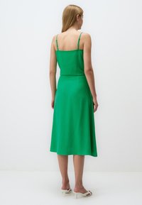 Robe sans manches verte avec un corsage ajusté et une jupe évasée, fabriquée dans un tissu léger. Présente des bretelles fines et un design mi-long.