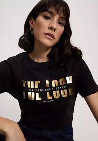 Czarna koszulka z krótkim rękawem z złotym nadrukiem "WYGLĄD FANTASTYCZNEGO STYLU CROSS JEANS". Gładki materiał i luźny krój.