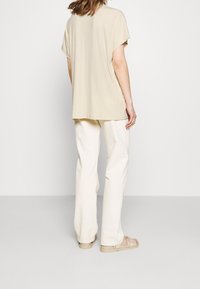 Beige kortärmad topp i texturerat tyg, kombinerad med krämfärgade, löst sittande byxor och ljusfärgade sandaler. Enkel design och ledig passform.