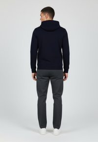 Felpa con cappuccio blu navy in tessuto testurizzato, con polsini a costine e vestibilità rilassata, abbinata a pantaloni grigio scuro e sneakers bianche.