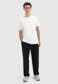 Witte katoenen t-shirt met korte mouwen en zwarte tekst "PUNK PARTY", gecombineerd met zwarte losse broeken en lichtgrijze sneakers.