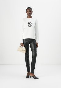 Vit sweatshirts med en tecknad hundgrafik; kombinerat med svarta konstläderbyxor och spetsiga svarta klackar. Beige handväska med logotyp.