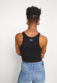 Débardeur noir à côtes avec un décolleté arrondi, associé à un jean taille haute bleu clair. Présente une petite étiquette de marque sur le dos en haut.