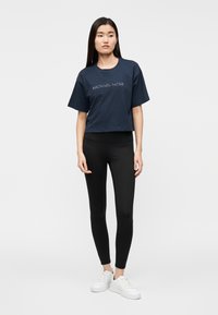 T-shirt azul-marinho cropped com o logótipo "MICHAEL KORS" em texto claro, combinada com leggings pretas e ténis brancos com solas texturizadas.
