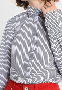 Camisa de botones a rayas blancas y azul marino con cuello, que presenta mangas largas y una textura suave. Botones en los puños y la tapeta.