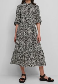 Zwart-wit midi-jurk met patroon, pofmouwen, elastische tailleband en een rok met meerdere lagen. Gecombineerd met zwarte sandalen met bandjes.