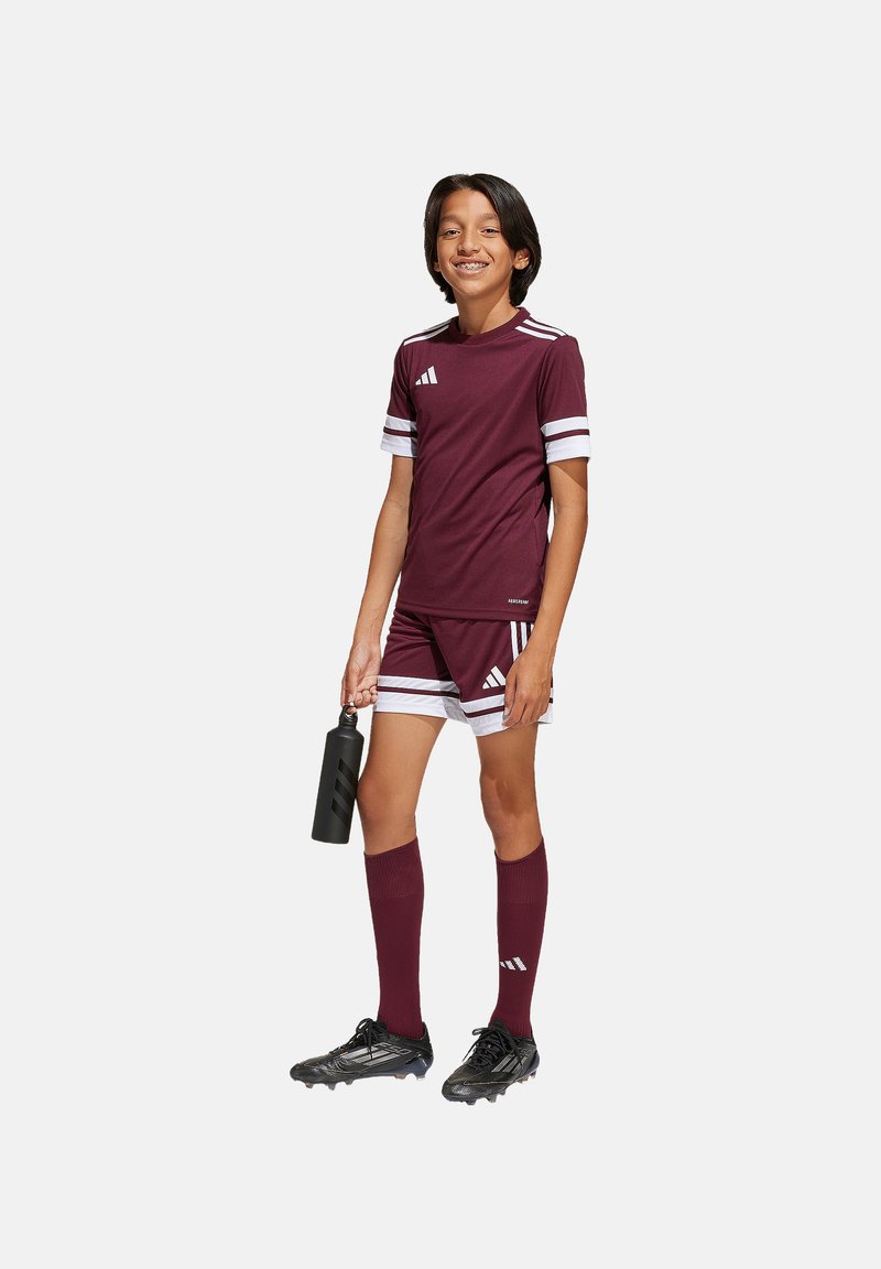Burgunderfarbenes Fußballtrikot mit weißen Streifen, bestehend aus einem kurzärmligen Shirt und Shorts, kombiniert mit knielangen Socken und schwarzen Fußballschuhen.
