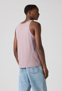 Top sem mangas, de tom mauve claro, feito de algodão, com decote redondo e design simples, combinado com jeans de denim de corte relaxado em azul claro.