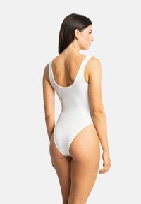 Maillot de bain une pièce blanc à côtes avec un dos dégagé, de larges bretelles et des jambes à forte échancrure, mettant en valeur une silhouette lisse et ajustée.