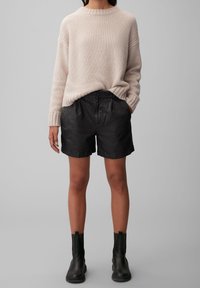 Světlý béžový pletený svetr s kulatým výstřihem, doplněný černými koženými šortkami s volným střihem a ohrnutými manžetami. Černé kotníkové boty.