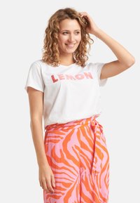 Witte katoenen t-shirt met "LEMON" in het roze gedrukt, gecombineerd met roze broek met een oranje zebra-strepenpatroon en een gestrikt tailleband.