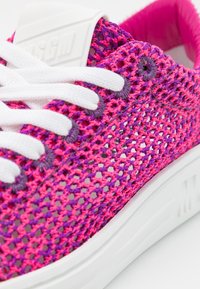 Baskets tricotées roses et violettes avec des lacets blancs, présentant une texture en maille respirante et une semelle blanche unie. Logo de marque notable sur la languette.