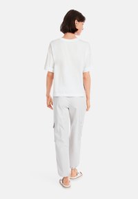 White short-sleeve T-shirt with rolled cuffs paired with light gray cargo pants featuring side pockets and elastic cuffs, worn with sandals.