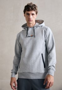 Pelēks džemperis no mīkstas auduma ar rāvējslēdzēja kabatu, regulējamu kapuci un ribinātām piedurknēm. Uz krūtīm ir izšūts logo.