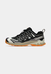 Black athletic shoe with grey and white accents, features a textured sole and orange outsole. Lacing system provides a secure fit.