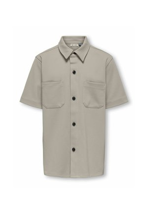Chemise beige à manches courtes avec un col pointu, quatre boutons noirs et deux poches poitrine avant avec rabats.